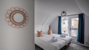 Hotellihuone, jossa on sänky, kaksi tyynyä, pyyhe, lamppu ja ikkunasta avautuva näkymä, ikkunassa on verhot.