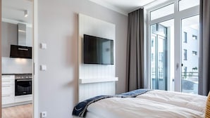 A modern hotel room with a bed, a TV mounted on the wall, a kitchen area, and large windows. - 4 Star Holiday Home in Travemunde (Lübeck)
