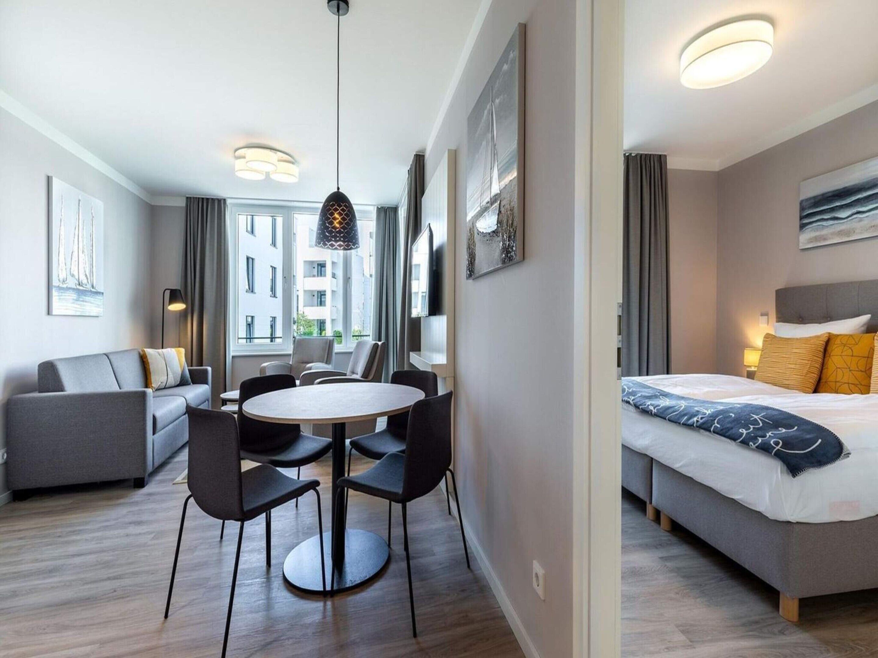 A modern hotel room with a bed, a seating area with a table and chairs, a large window, and artwork on the walls.