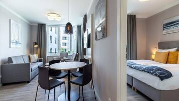 A modern hotel room with a bed, a seating area with a table and chairs, a large window, and artwork on the walls.