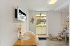 Ein modernes Interieur mit einem Holzesstisch, einem an der Wand montierten Fernseher, einem kleinen weißen Stuhl und einer Treppe mit Holzsitzgelegenheiten.
