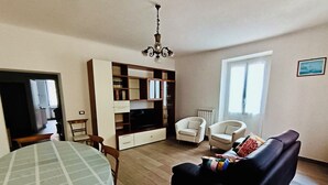 En stue med spisebord, to lænestole, en sofa, et fjernsyn og en reol.