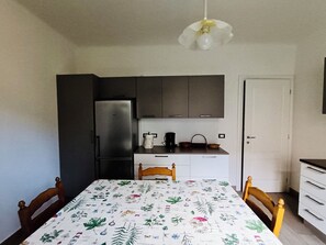 A compact kitchen with a refrigerator, a coffee maker, and a sink. There is a dining table with chairs and a ceiling light fixture. - Camogli. Cozy apartment only 5 minutes from the sea (Camogli)