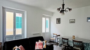 En stue med en sort sofa, et spisebord med stole og en lysekrone.