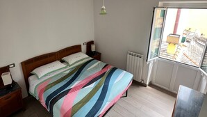 Et soveværelse med seng, to sengeborde, en radiator, et vindue med udsigt og en hængende lampe.
