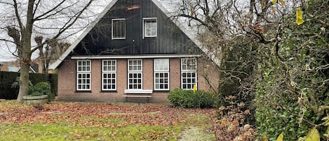 En traditionell byggnad med svart tak, symmetrisk fasad, en central entré och en liten veranda.