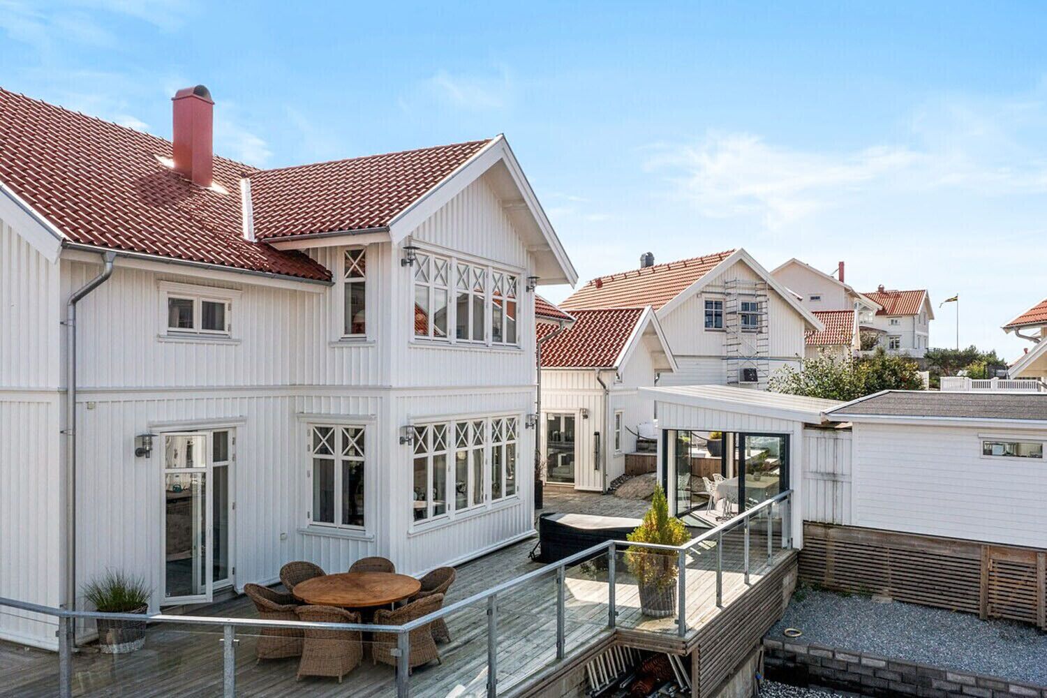 Ein weißes, zweistöckiges Haus mit rotem Ziegeldach, einem Balkon mit Korbmöbeln und einer Glasveranda.