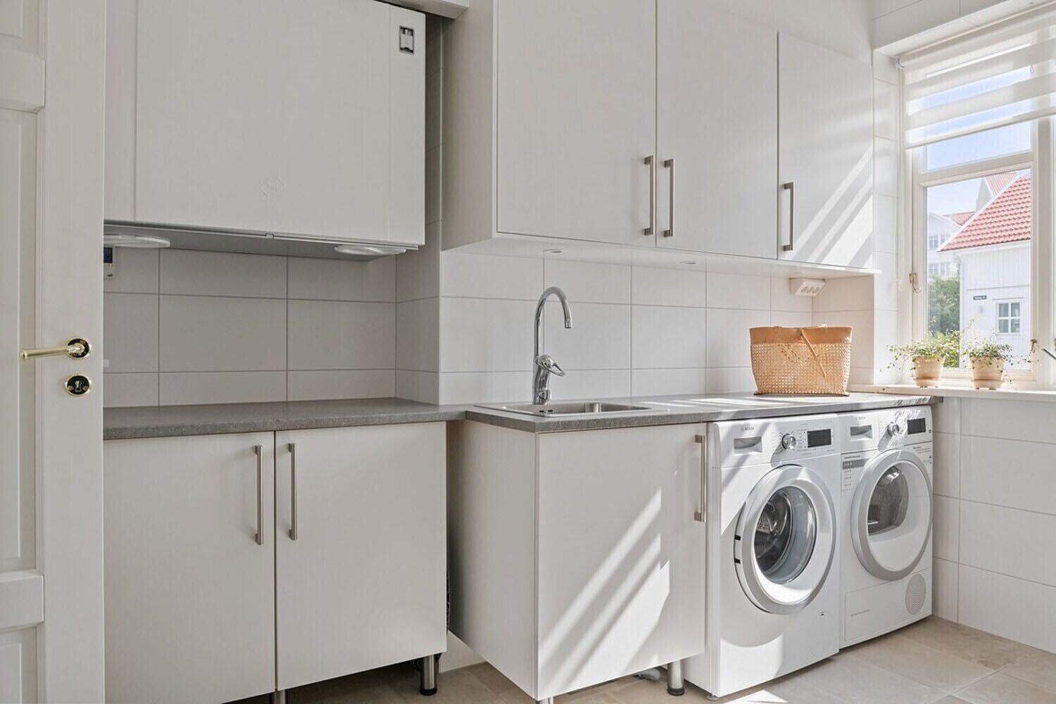 Una cocina moderna con armarios blancos, lavadora integrada, un lavamanos y una ventana con vistas a edificios.