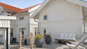 Valkoinen rakennus, jossa on punainen katto, ulkotila istumiseen ja ruukuissa olevia kasveja.