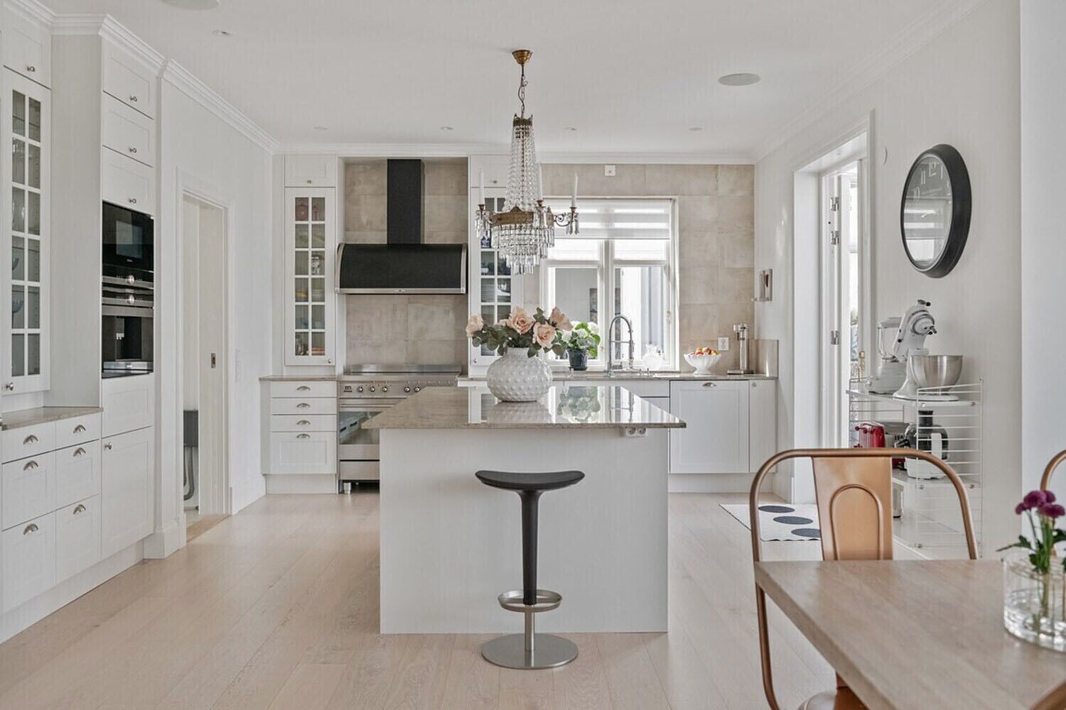 A modern kitchen with white cabinetry, a central island, a chandelier, and a dining area with a chair and table.