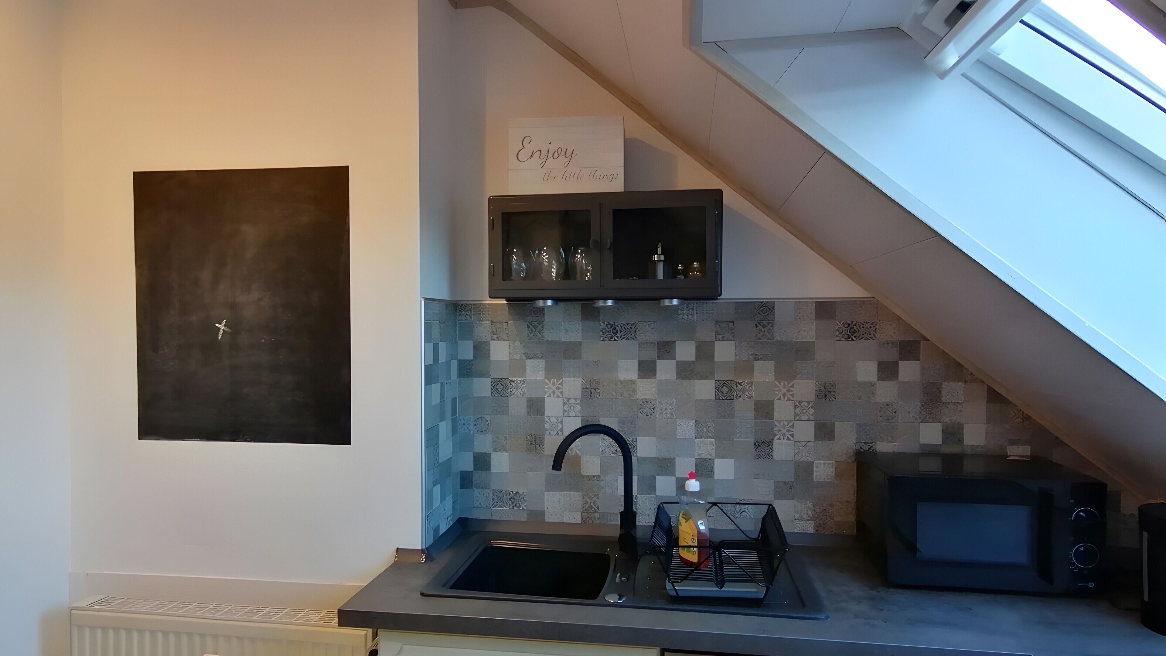 A kitchen with a tiled backsplash, a black sink, a microwave, and a cabinet above the sink.