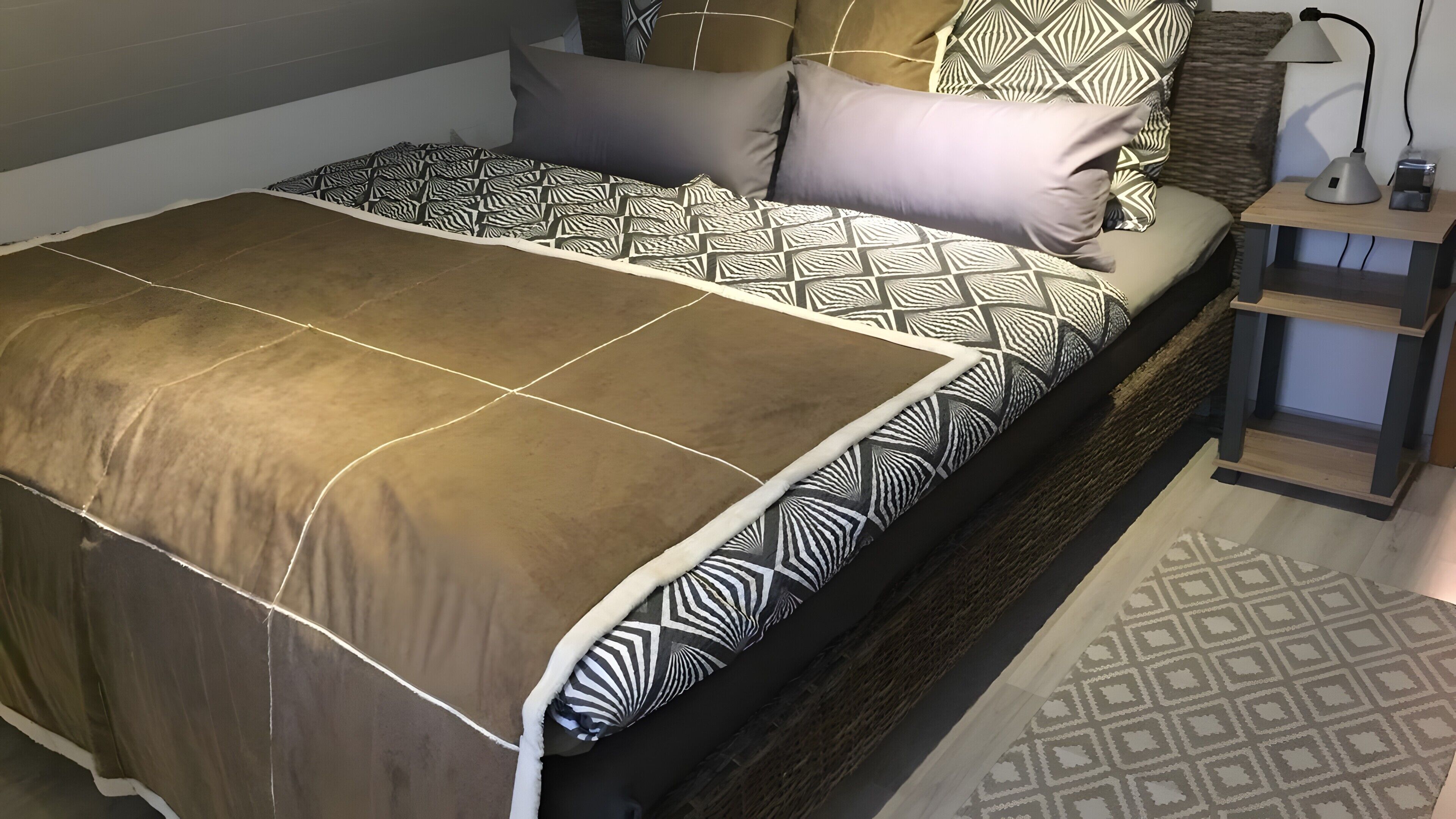 Un lit avec une literie à motifs, une table de chevet avec une lampe et un tapis à motifs.