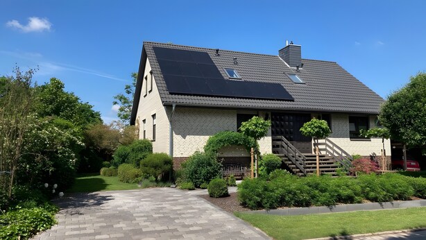 Una casa con tetto spiovente, pannelli solari, un ingresso principale con gradini e una strada privata.