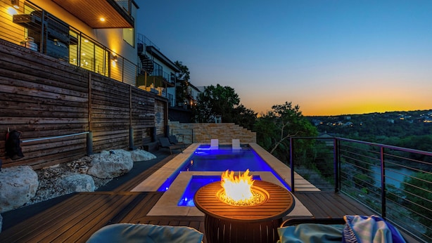 En moderne udendørs terrasse med jacuzzi, træterrasse og udsigt over byen i skumringen.