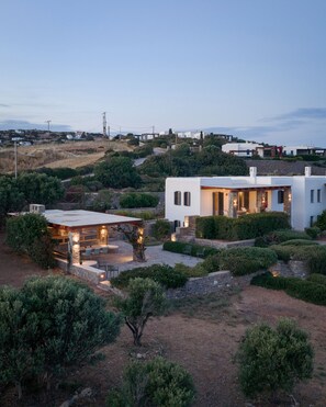 Ein modernes Haus mit Terrasse, umgeben von Grünflächen und Hügeln im Hintergrund.