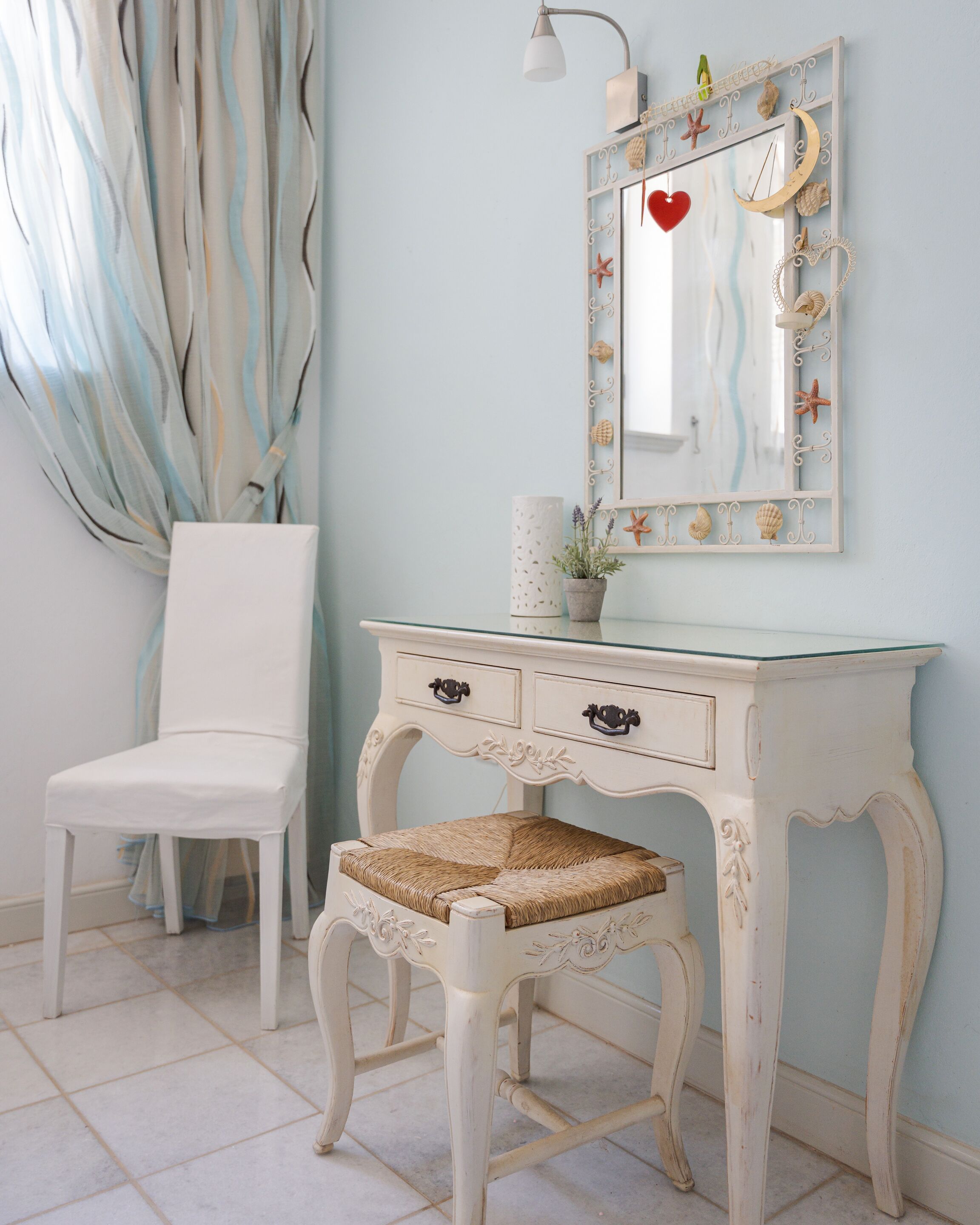A white vanity with a mirror, a chair, and a decorative wall with a heart and seashells.