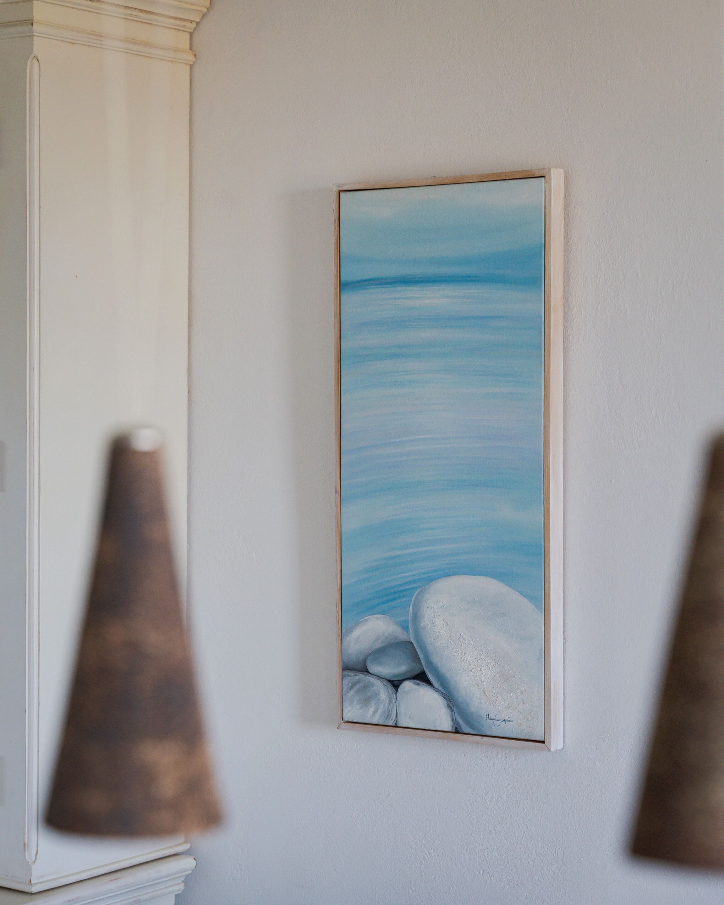 Ein Gemälde von ruhiger See mit Felsen an einer weißen Wand.