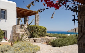 Ein Steinhaus mit einer Holzpergola, einer Steintreppe und Blick auf das Meer.