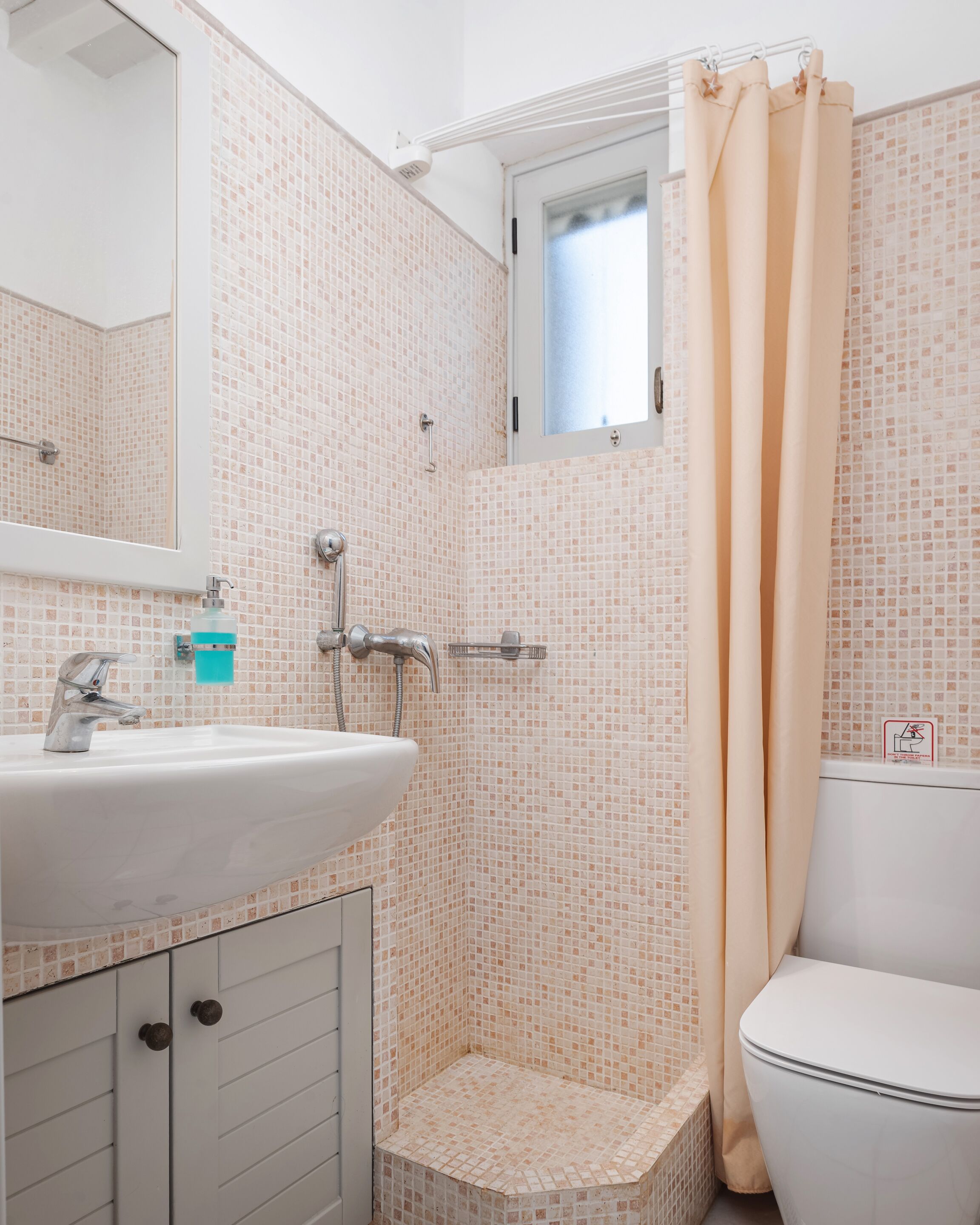 A bathroom with a shower, toilet, sink, and a window.