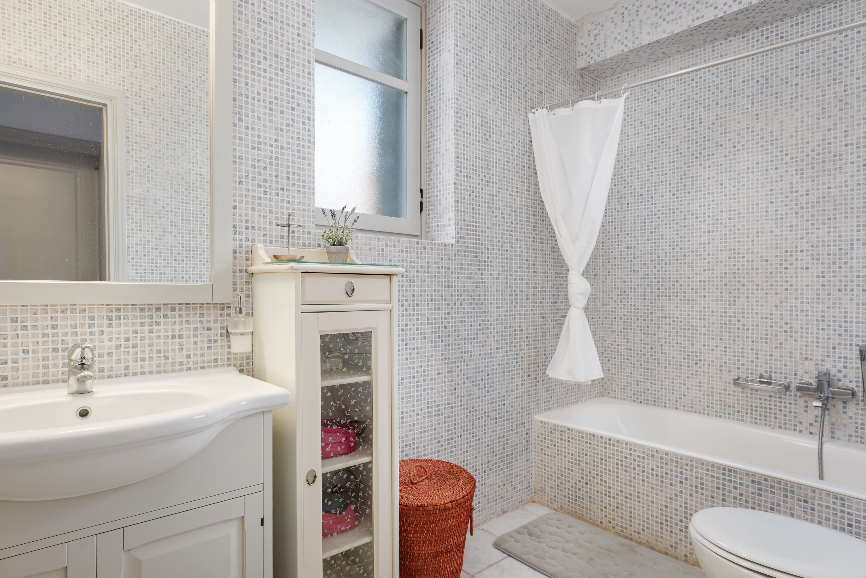 A bathroom with a white sink, a mirror, a window, a shower curtain, and a bathtub.