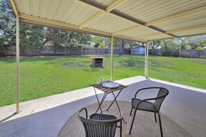 Un patio techado con mesa y sillas, una parrilla y un jardín cubierto de césped.