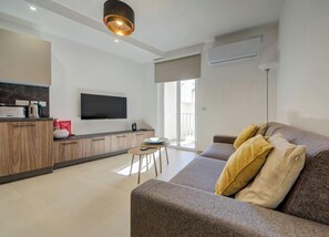 A modern living room with a sofa, a coffee table, and a flat-screen TV mounted on the wall. - Stylish 2BR Retreat w/ Balcony & Fast WiFi (Msida)