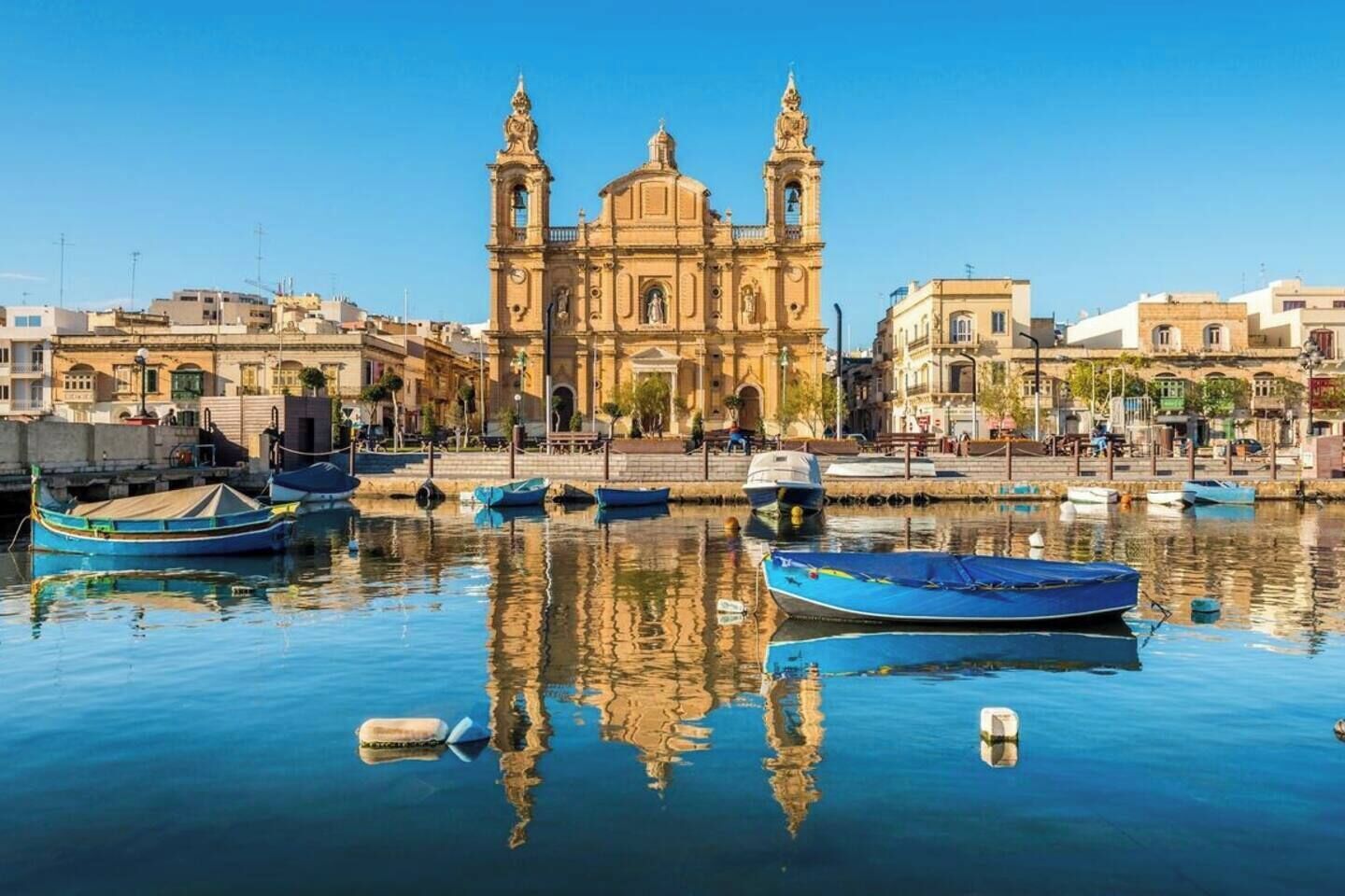 Un edificio storico con due torri, un lungomare e diverse imbarcazioni.