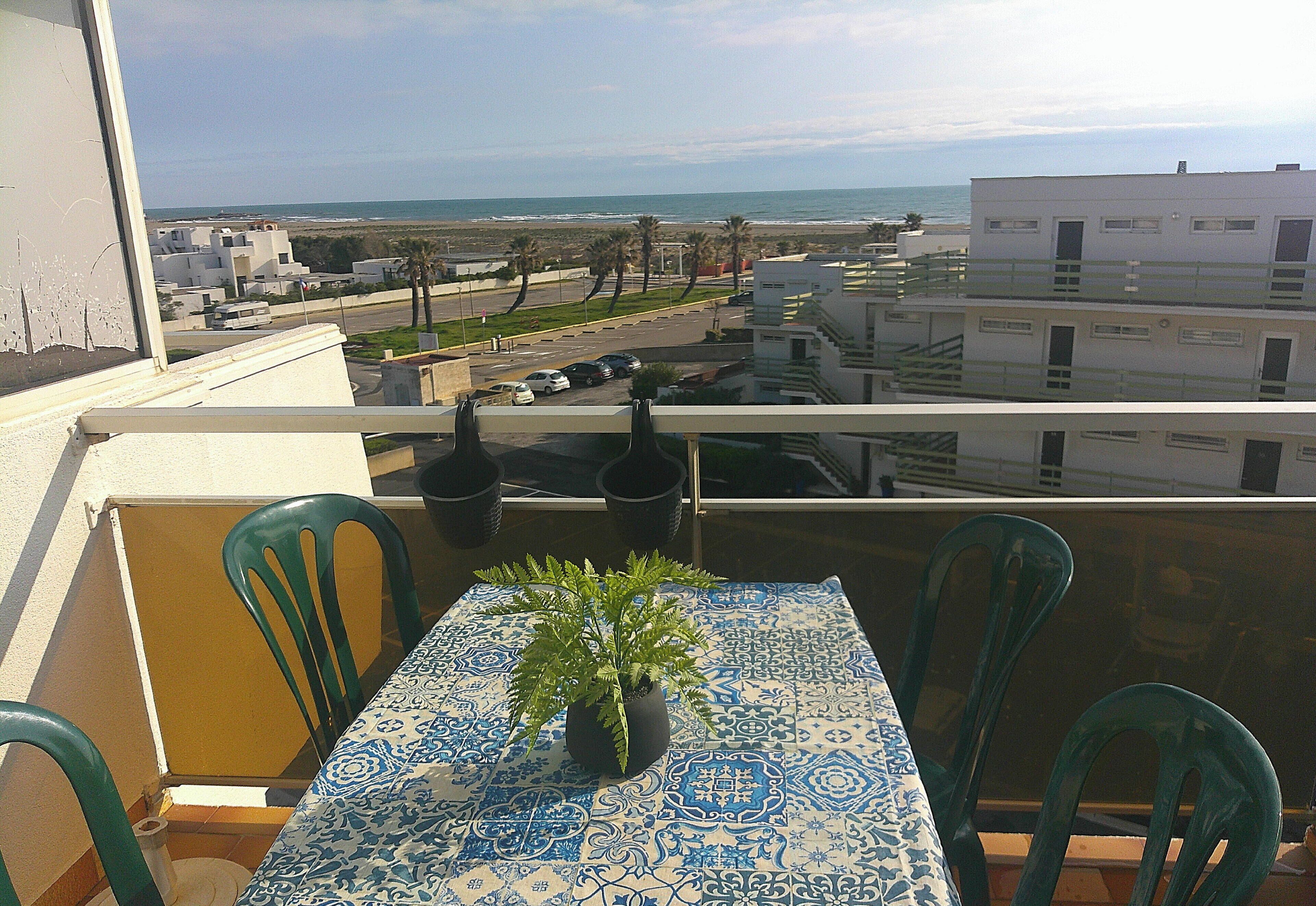 A balcony with a table, chairs, and a potted plant.