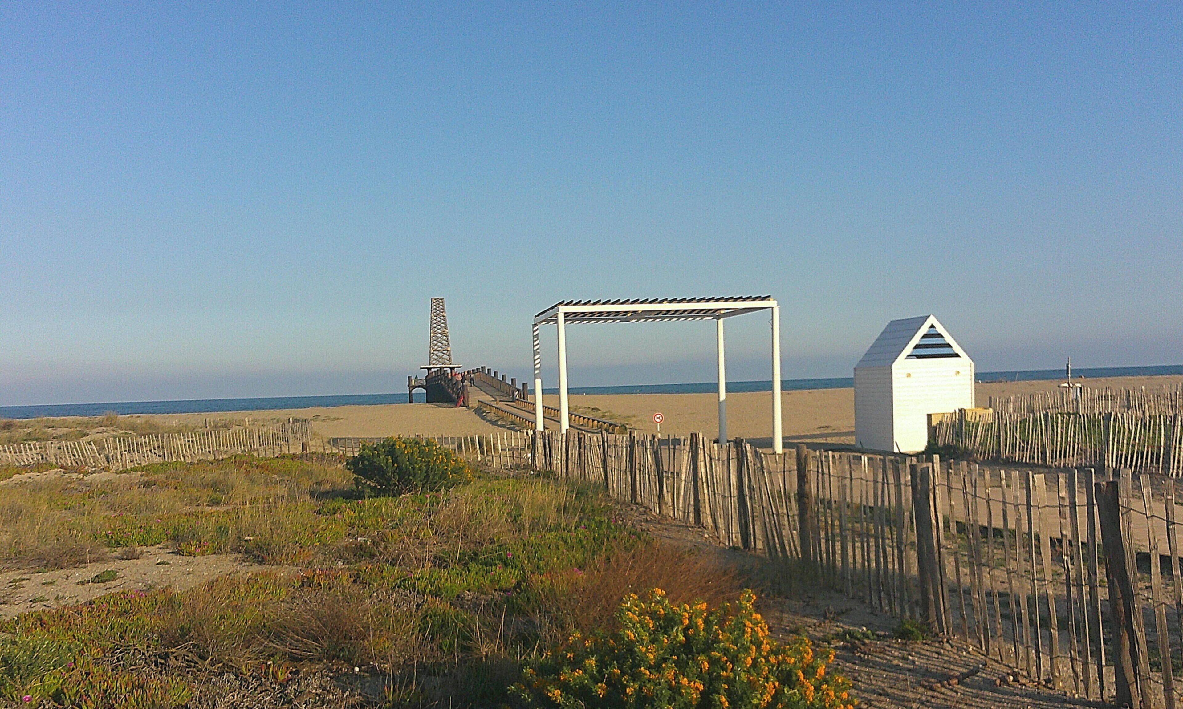Une plage avec une clôture en bois, une structure blanche et un monument imposant.