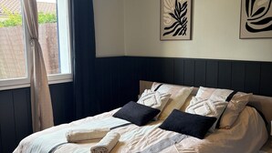 A neatly made bed with a headboard, a window with curtains, and wall art.