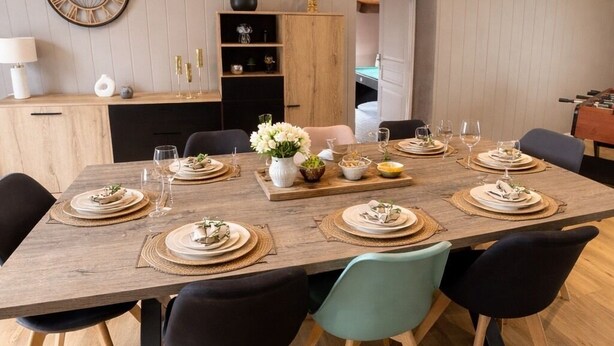 A dining area with a wooden table set for six, surrounded by black chairs.