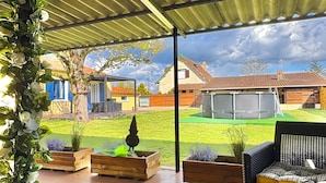 A covered patio with outdoor furniture, planters, and a view of a residential area.