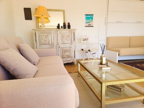 A living room with a beige sofa, a glass coffee table, a white cabinet with decorative items, and a poster on the wall.