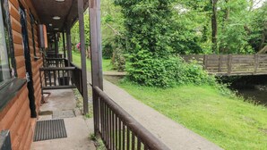 Een houten hutje met een overdekte veranda, een betonnen pad en een gazon met een houten brug.
