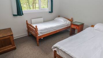 Un dormitorio con una cama individual, una mesita de noche, una mesita auxiliar de madera, un radiador y una ventana con cortinas.
