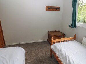 Un dormitorio con dos camas individuales, una mesita de noche de madera, un estante pequeño de madera y una ventana con cortinas.