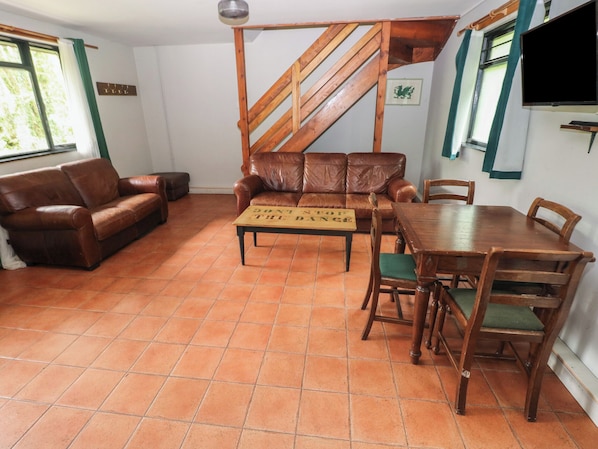 Una sala de estar con una escalera de madera, un sofá de cuero marrón, una mesa de comedor de madera con sillas y un letrero sobre la mesa.