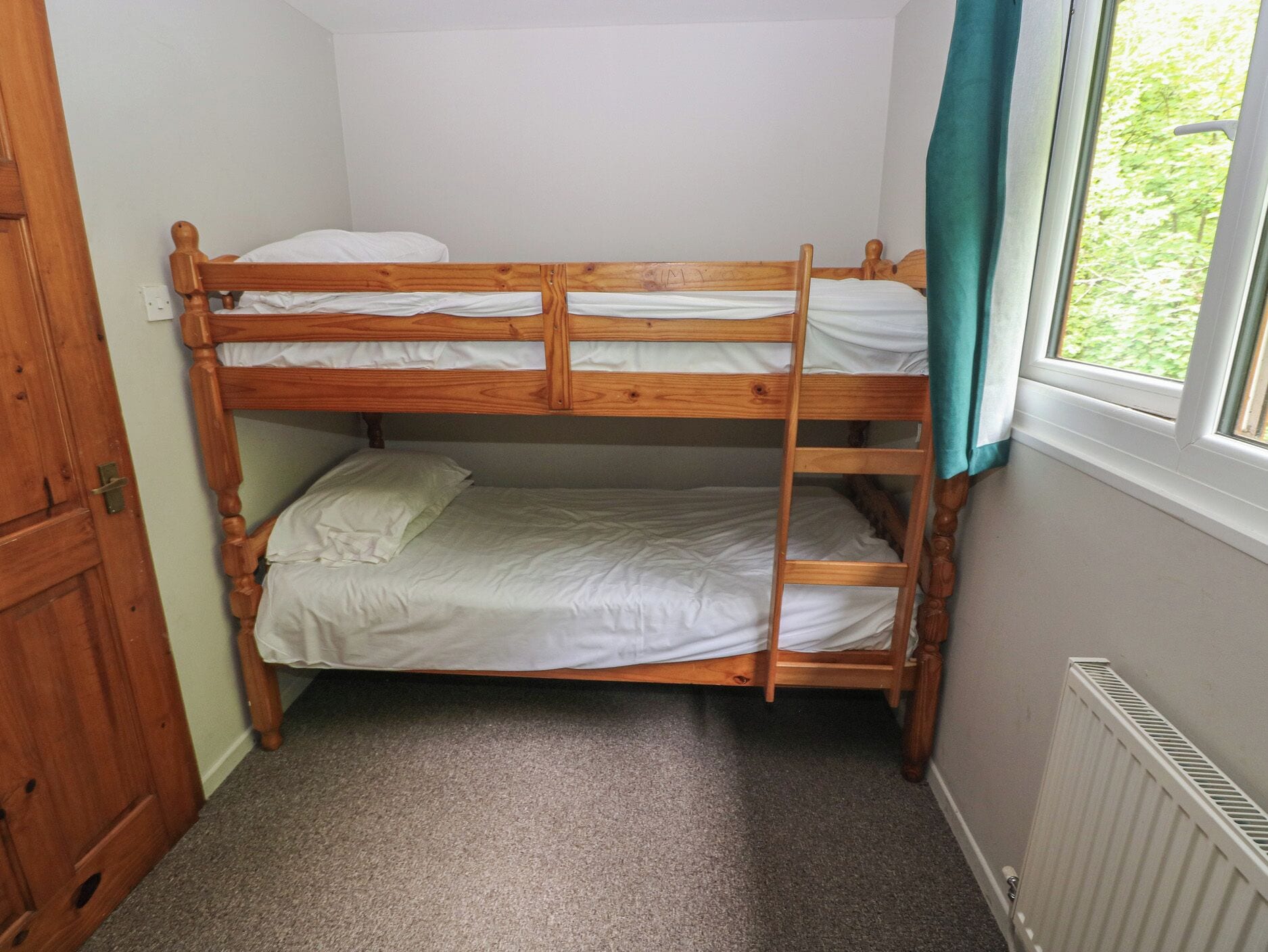 Ein Stockbett in einem Zimmer mit Fenster, Teppichboden und Heizkörper.
