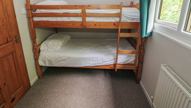 Een stapelbed in een kamer met een raam, tapijtvloer en een radiator.