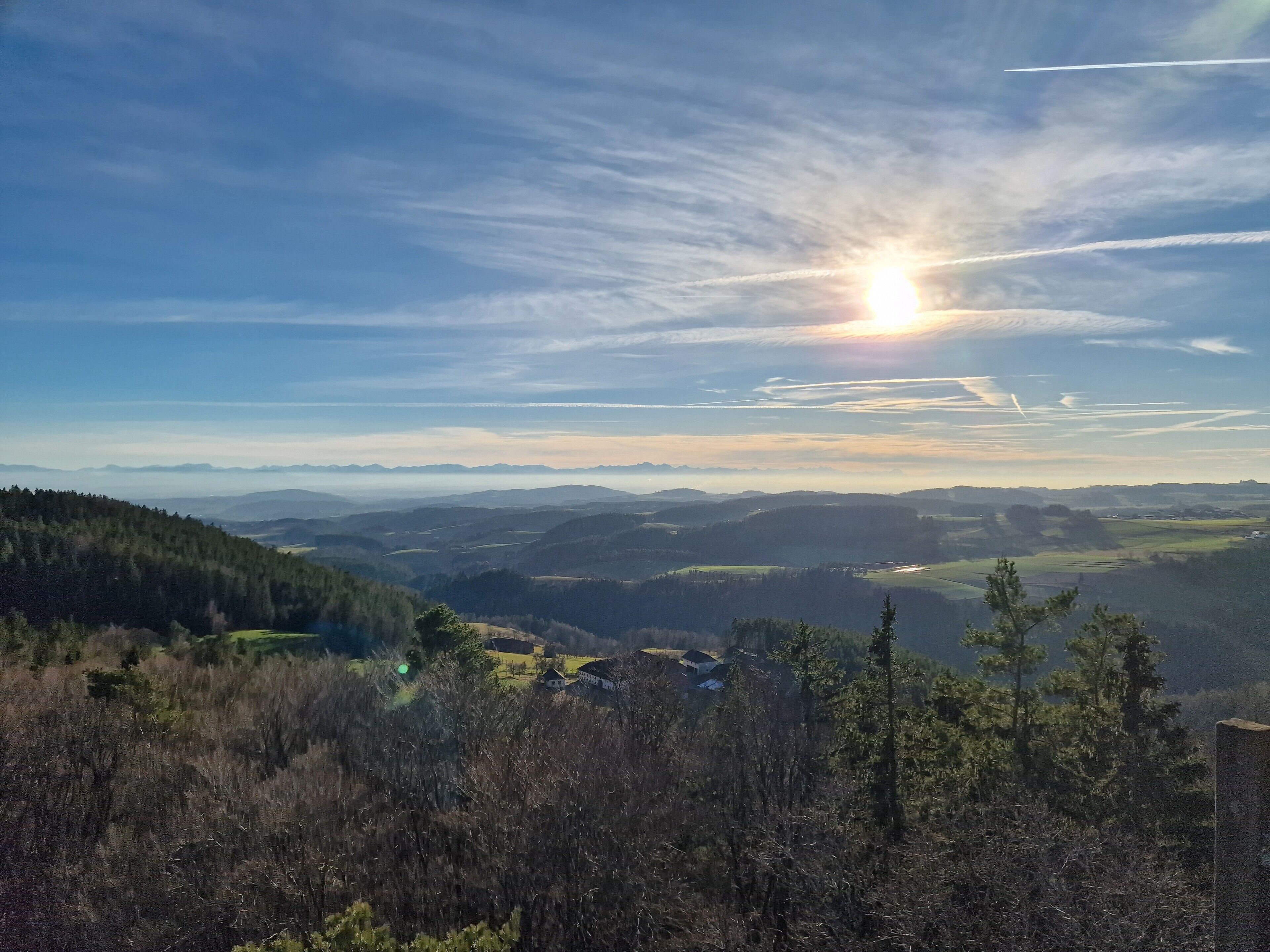 A panoramic view of a mountainous landscape with a clear sky and the sun setting or rising.