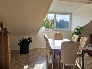 A dining area with a table and chairs, a potted plant, and a view of trees through a window.