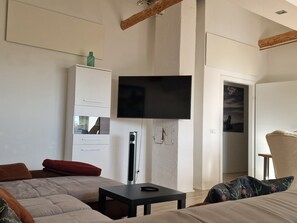A bedroom with a bed, a TV mounted on the wall, a wardrobe, and a door leading to another room.