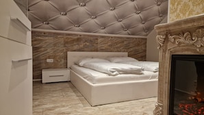 Une chambre à coucher avec une tête de lit capitonnée, un lit, une table de chevet, une commode et une cheminée.