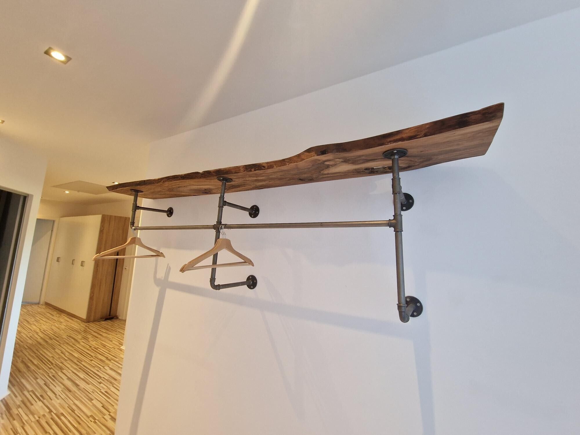 A hallway with a wooden beam ceiling, a metal rack with hangers, and a wooden floor.