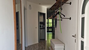 Un couloir avec un plancher en bois, un tapis bleu, un banc, un porte-manteau et une porte donnant sur une cuisine.