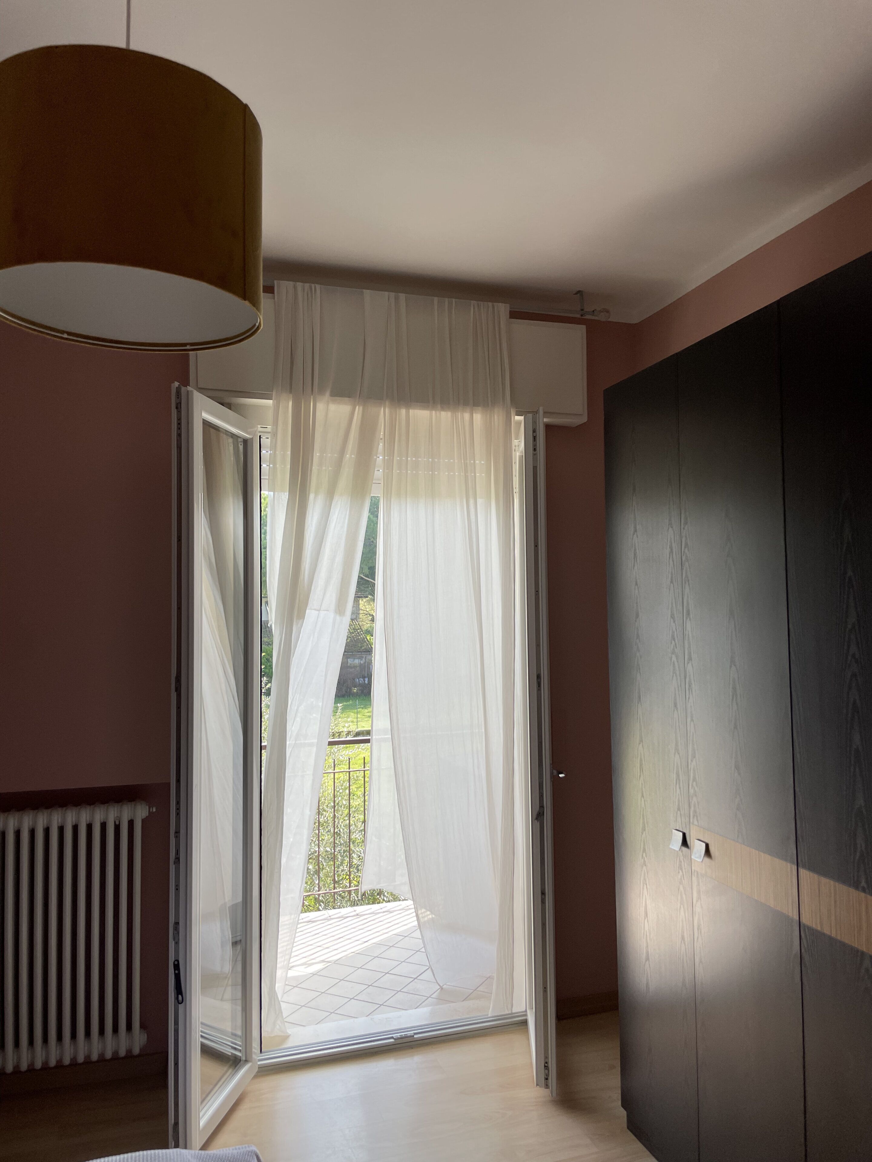 Une pièce dotée d’une porte-fenêtre coulissante donnant sur un balcon, d’un radiateur et d’une grande armoire.