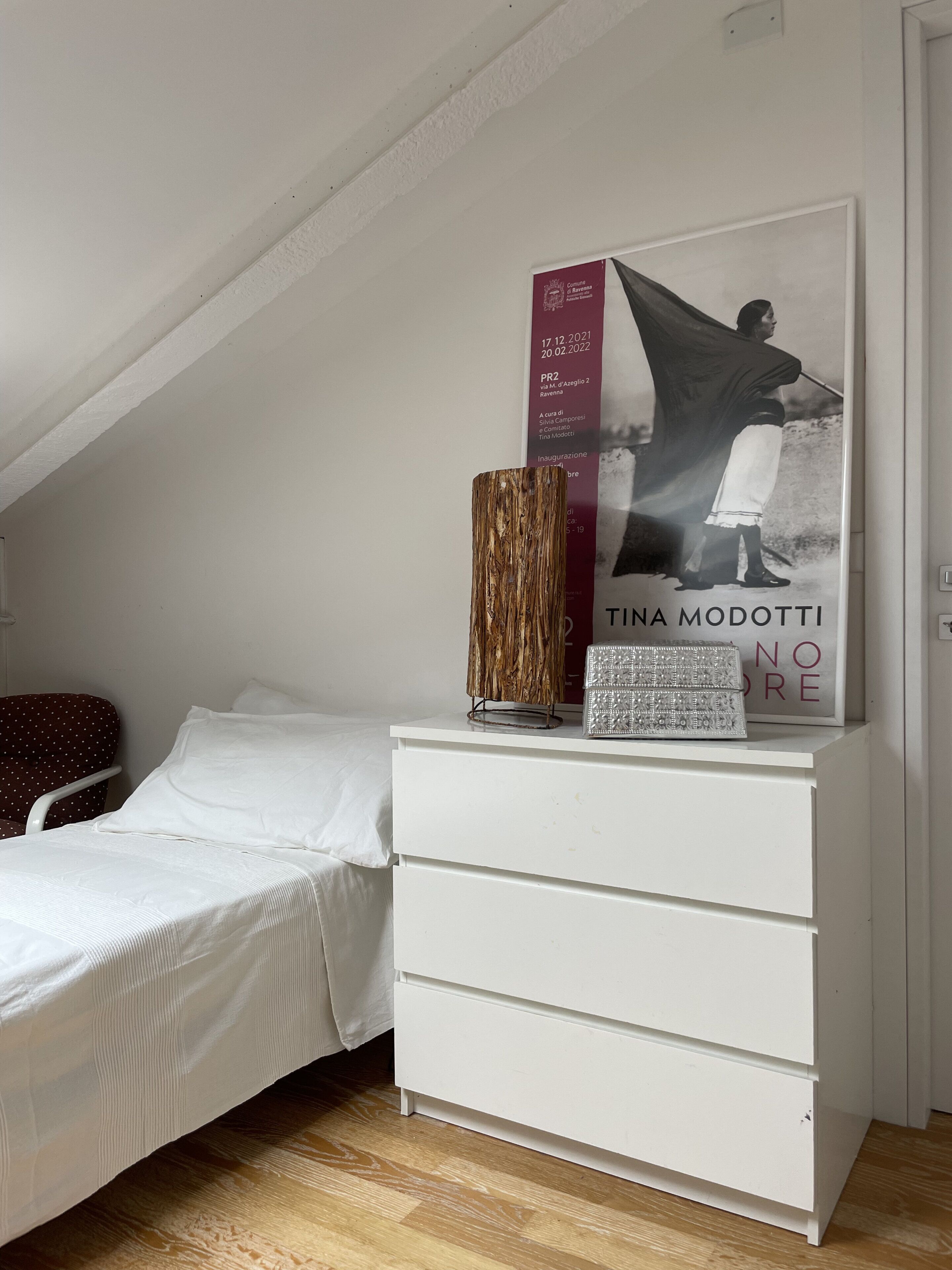 Une chambre à coucher avec un lit, une commode blanche et une affiche accrochée au mur.