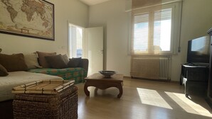 Uma sala de estar com um sofá, uma cesta de vime, uma mesa de centro de madeira, um mapa-múndi na parede e uma televisão.
