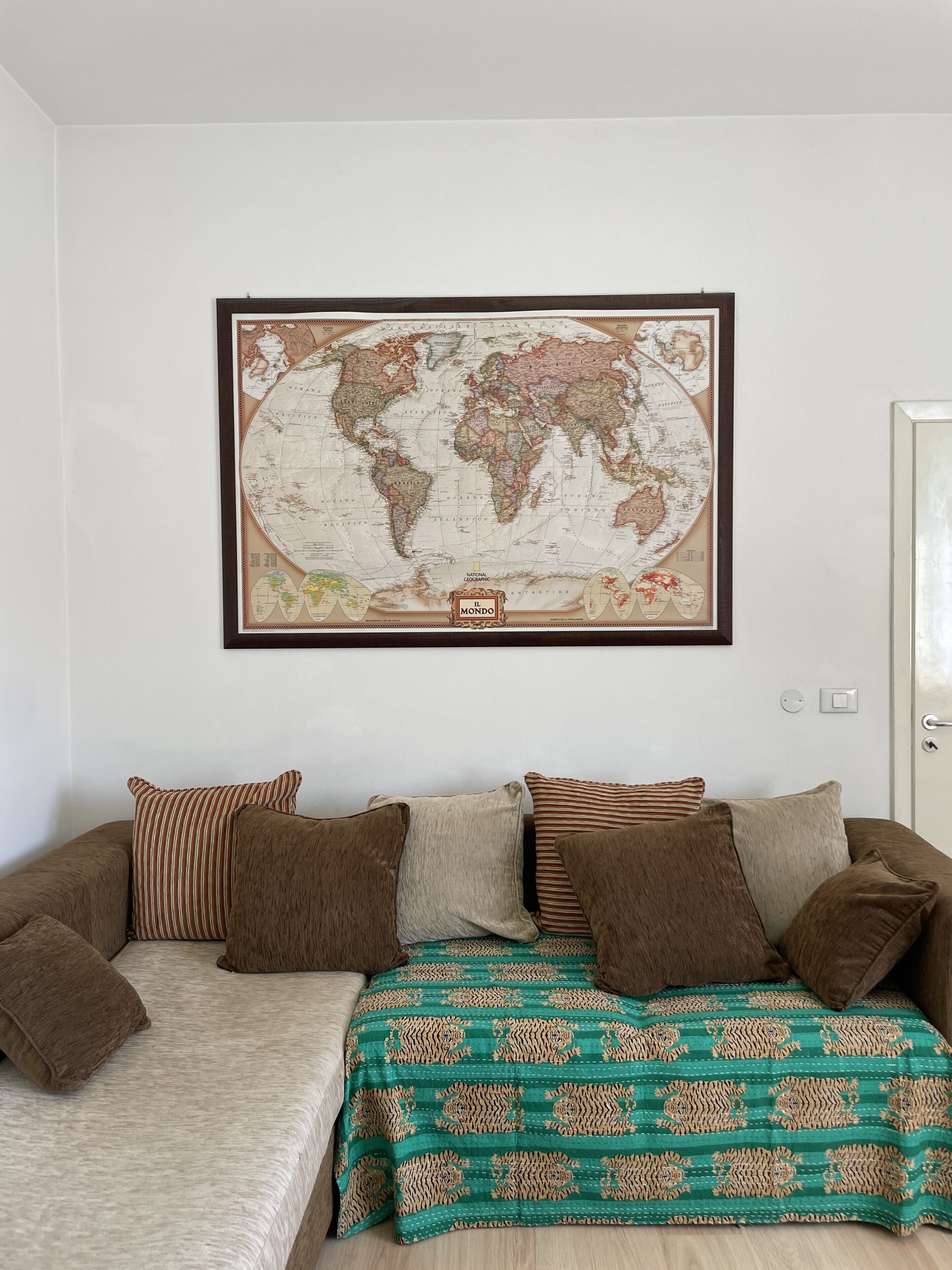 Une pièce avec une grande carte du monde accrochée au mur, un canapé marron orné de coussins à motifs et un plaid vert à motifs.