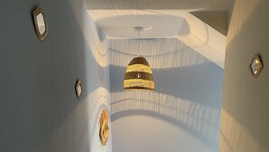 Um corredor estreito com teto estampado, luminária pendente, um objeto decorativo na parede e um vaso sobre um tapete.